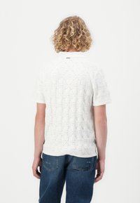 Witte korte mouwen shirt met een textuur en geborduurd patroon dat vierkante uitsparingen bevat. De achterkant toont een effen kleur kraag en een casual pasvorm.