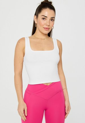 Weißes, geripptes Tanktop mit quadratischem Ausschnitt, kombiniert mit pinken, hoch taillierten Leggings mit einem Überkreuz-Design und Nähdetails.