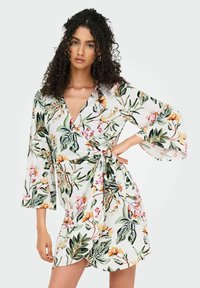 Blumenkleid mit tiefem V-Ausschnitt, Glockenärmeln und Bindegürtel. Mit bunten botanischen Drucken auf weißem Hintergrund.