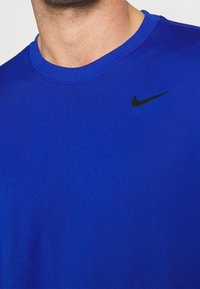 Man som bär en kungablå t-shirt med rund halsringning från Nike, med en liten svart Nike-swoosh-logotyp på vänster bröst.