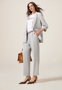 Completo grigio chiaro con blazer su misura e pantaloni dritti. Abbinato a una maglietta bianca con la scritta "PARIS" in lettere metalliche e tacchi leopardati.
