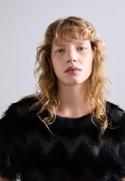 Mustaga tekstuuriga topp, mis sisaldab franje aktsente ja chevron mustrit, ümmarguse kaelusega ning läbipaistvast kangast. Kujundus rõhutab kihte ja liikumist.