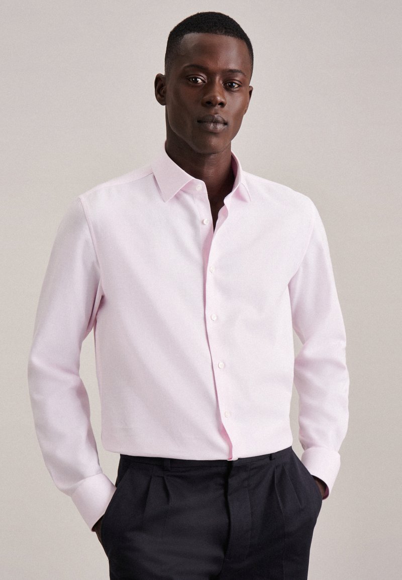 Chemise à manches longues rose clair avec un col, fabriquée en tissu lisse. Présente une coupe droite et de subtils accents roses près des boutons.