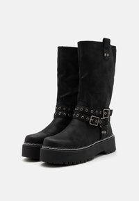 Botas negras hasta la rodilla, hechas de un material suave, con detalles de hebilla y clavos, una suela de plataforma gruesa y acentos de costura blanca.