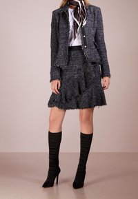 Czarna tweedowa marynarka z postrzępionymi brzegami, w zestawie z dopasowaną spódnicą z falbanami. Modelka nosi czarne skarpetkowe kozaki do kolan.