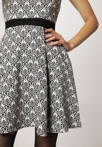 Abito a righe bianche e nere con corpetto aderente, gonna a campana e una cintura nera. Tessuto liscio con intricati disegni a spirale.