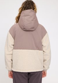 Padded jacket in beige and light brown, featuring a hoodie, soft textured fleece material, and contrasting color blocks on the back.