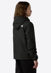 Veste noire imperméable avec capuche, poignets élastiques et logo dans le dos. Texture lisse et coupe droite.
