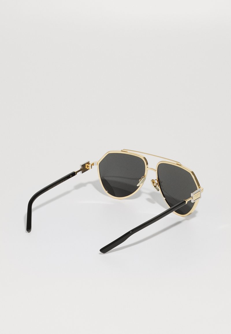 Óculos de sol com armação dourada e lentes pretas em formato octagonal, apresentando uma ponte dupla e hastes pretas elegantes com acabamento brilhante.