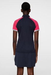 Marinblå polo-klänning med korta rosa raglanärmar, texturerad tyg och en utsvängd kjol. Har en logotyp längs ärmkanterna.