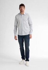 Bílá košile na knoflíky s drobnými modrými vzory, kombinovaná s tmavě modrými džínami a bílými teniskami. Slim fit, dlouhé rukávy.