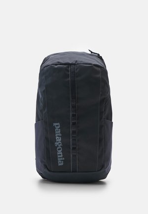 Zwarte rugzak met een gladde textuur, voorzien van een centrale rits, zijnetvakken en een opvallend logo aan de voorkant.