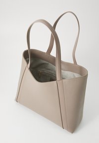 Light beige tote bag with a structured design, smooth leather exterior, dual handles, and a soft interior lining. Features an interior pocket.