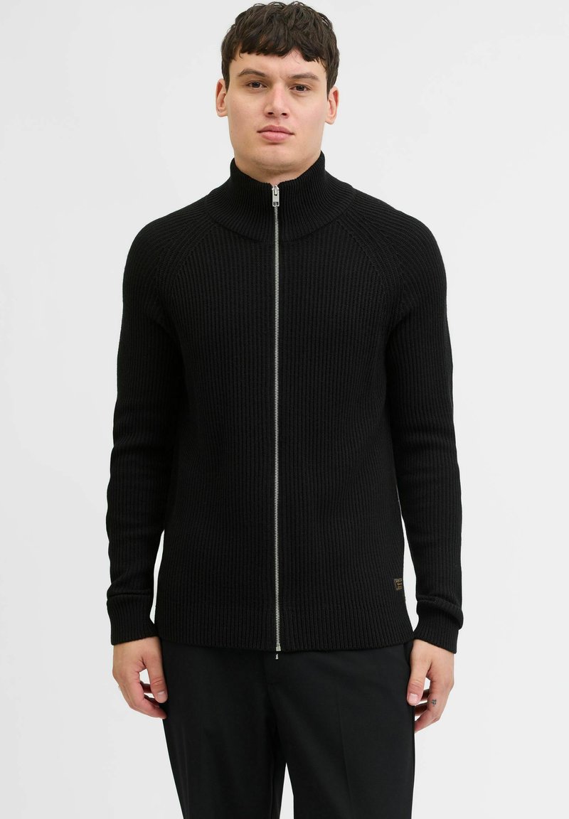 Sort ribbet zip-up trøje med høj krave, tætsiddende silhuet og lange ærmer. Har en metal lynlås og et lille logo mærke nær kanten.