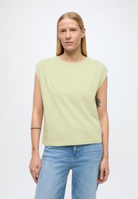 Haut vert clair à manches courtes avec une coupe décontractée. Tissu doux, encolure ronde et surpiqûres visibles. Associé à un jean bleu clair.