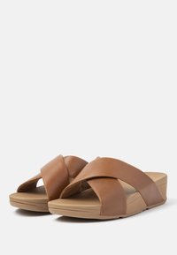 Bruine leren slide sandalen met gekruiste bandjes, een gevoerd voetbed en een tankleurige zool, voorzien van een sleehak voor extra hoogte.