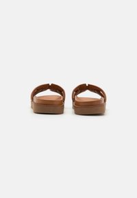 Sandali in pelle marrone con un design semplice, dotati di una suola piatta e due ampie cinghie. La texture è liscia con una finitura opaca.