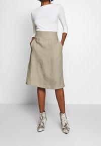 Beige linnkjol med sidofickor, knä-lång, med en åtsittande midja. I kombination med en vit ribbad topp och anklar boots i ormskinnsmönster.