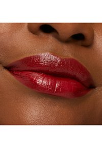 Crimson lipstick applied to full lips, glossy finish with subtle texture, set against smooth, medium brown skin.