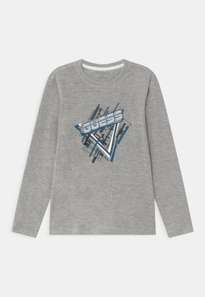 Chemise grise à manches longues avec un motif géométrique abstrait bleu et noir et le mot "GUESS" imprimé en lettres stylisées sur le devant.