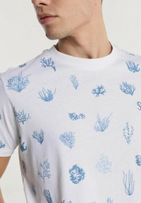 Weißes Baumwoll-T-Shirt mit einem durchgehenden Druck verschiedener blauer Korallendesigns. Das Shirt hat einen Rundhalsausschnitt und kurze Ärmel.