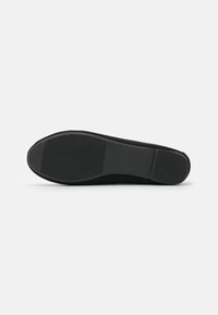 Sola nera di una scarpa con una texture liscia e opaca, caratterizzata da un motivo rigato per una maggiore aderenza e un tacco leggermente sollevato.