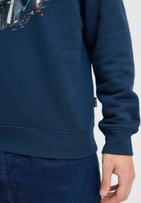 Sudadera azul marino con puños y dobladillo acanalados. Presenta un estampado gráfico en la parte frontal, fabricada con una tela suave y duradera.