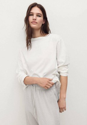 Blusa blanca de manga larga con escote redondo, combinada con pantalones grises claros texturizados que cuentan con una cintura elástica y cordón.
