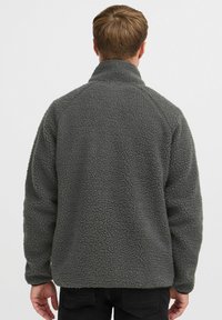 Grauer Fleece-Pullover mit hohem Kragen, strukturierten Oberflächen und Raglanärmeln. Hat keine sichtbaren Verschlüsse oder Muster.