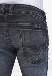Mörkblå denimjeans med en åtsittande design, synliga sömnadsdetaljer och en enda bakficka med en distinkt form och textur.