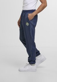 Pantaloni a righe blu navy realizzati in tessuto leggero, con vita e polsini elastici, e un logo ricamato sulla coscia sinistra.