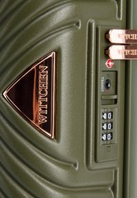 Maleta verde oliva con superficie texturizada, que cuenta con un logo en oro rosa, cerradura TSA y diales de combinación de cuatro dígitos para acceso seguro.