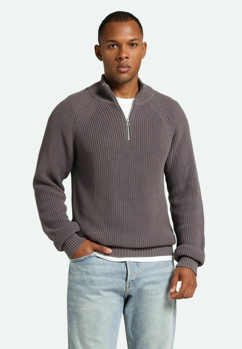Gray ribbed knit sweater with a quarter-zip collar, featuring raglan sleeves and a textured fabric. Paired with light blue jeans.