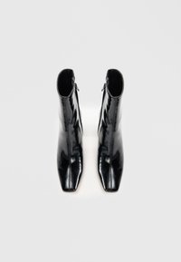 Botas de tobillo de charol negro con un diseño elegante de puntera afilada, que cuentan con un cierre lateral y una textura suave y brillante.