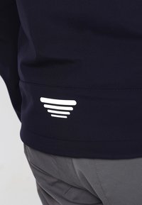 Sweatshirt bleu marine avec une texture lisse et un logo en ligne courbe blanche sur l'ourlet inférieur. Design simple, sans fermetures ni ornements.