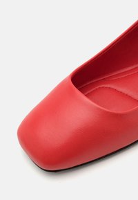 Zapato plano rojo con punta cuadrada, hecho de cuero suave. El interior tiene una textura suave, con un diseño minimalista y sin hardware visible.