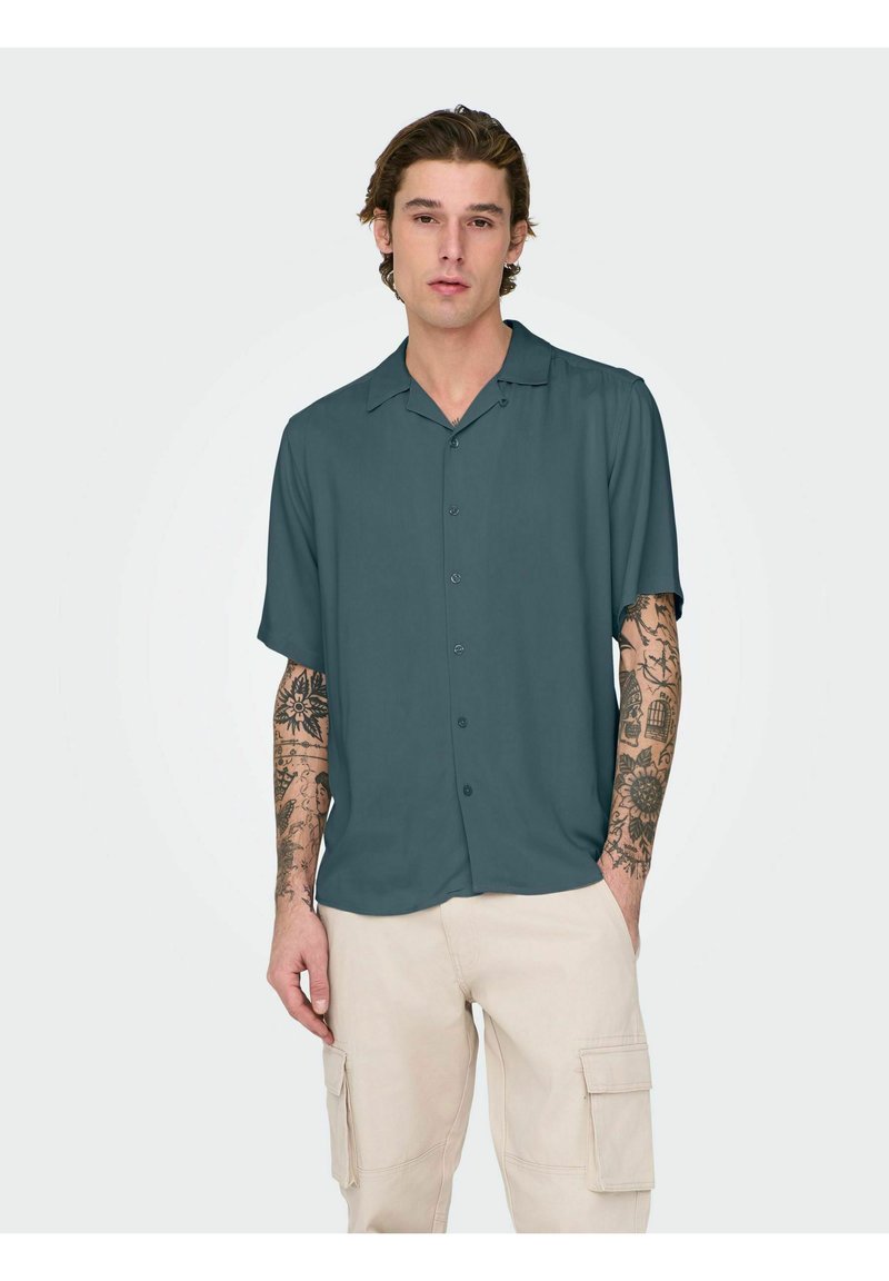 Short-sleeve, button-up shirt in dark teal fabric, featuring a camp collar, smooth texture, and worn with beige cargo shorts.