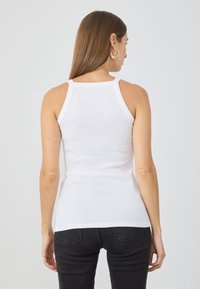 Top de tirantes de algodón blanco con un diseño ajustado, con tirantes anchos y un dobladillo recto, combinado con jeans negros.