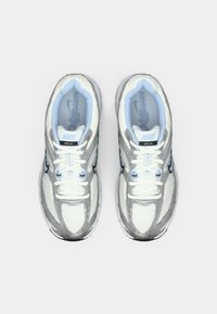 Buty Nike MOTO 2K, charakteryzujące się białą i srebrną siateczką, jasnoniebieskimi akcentami, odblaskowymi detalami oraz teksturowaną gumową podeszwą.