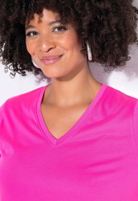 Rosa V-Ausschnitt-T-Shirt aus weichem Stoff, mit kurzen Ärmeln und glatter Textur, getragen von einer Person mit lockigem Haar.