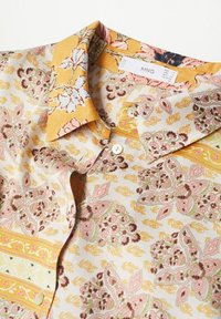 Blouse à manches longues en tissu léger à motifs floraux et cachemire. Couleurs comprenant le jaune, le rose et le vert avec fermeture par boutons.