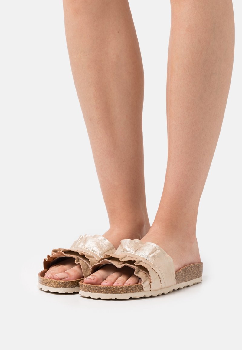 Sandales plates avec une semelle en liège, dotées de brides volantées en tissu métallique et doux en beige et marron clair. Design à bout ouvert pour une meilleure aération.