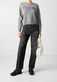Sudadera gris con la palabra "ATTITUDE" en letras texturizadas, combinada con jeans de mezclilla oscura, zapatillas deportivas negras y un bolso blanco.