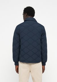 Marineblauer, gestepptes Jacke mit Wellenmuster, Kragen und gerippten Bündchen, hergestellt aus glattem, leichtem Stoff.