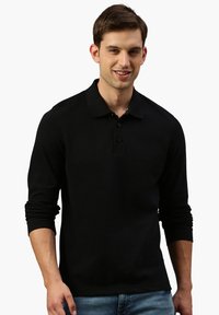 Schwarzes Langarm-Polohemd mit Kragen, drei-Knopf-Leiste, strukturiertem Stoff und enganliegenden Ärmeln, kombiniert mit blauen Denim-Jeans.