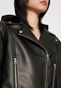 Černá kožená moto bunda s dvojitým zapínáním, stříbrnými zipy, patentkami a textura povrchem.