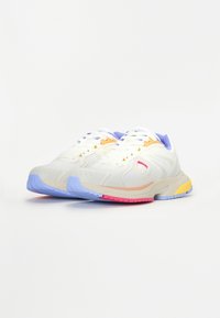 Chaussures de sport blanches avec une tige en mesh agrémentée d'accents pastel orange, violet et jaune, et une semelle en caoutchouc multicolore.