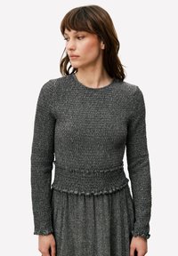 Pull gris à manches longues en maille avec une finition texturée, doté d'une taille froncée et de poignets à volants, porté par-dessus une robe assortie.