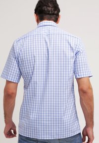 Lyhythihainen paita vaaleansinisessä ja valkoisessa ruutukuosissa, jossa on tavallinen kaulus ja sileä pinta, pyöristetty helma ja takana olkapään yläosa suunnittelu.