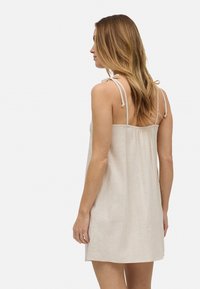Vestido de lino beige claro con tirantes ajustables en los hombros, corte relajado y espalda fruncida. Presenta una textura suave y un diseño minimalista.